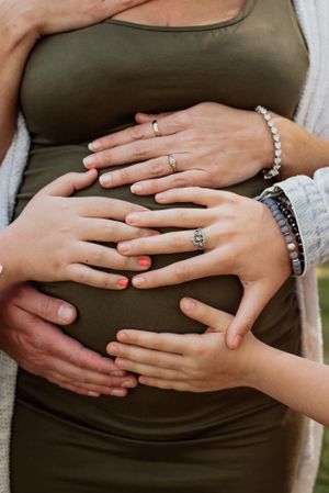 Multiple hands touching a pregnant belly wearing a green dress with jewelry visible.