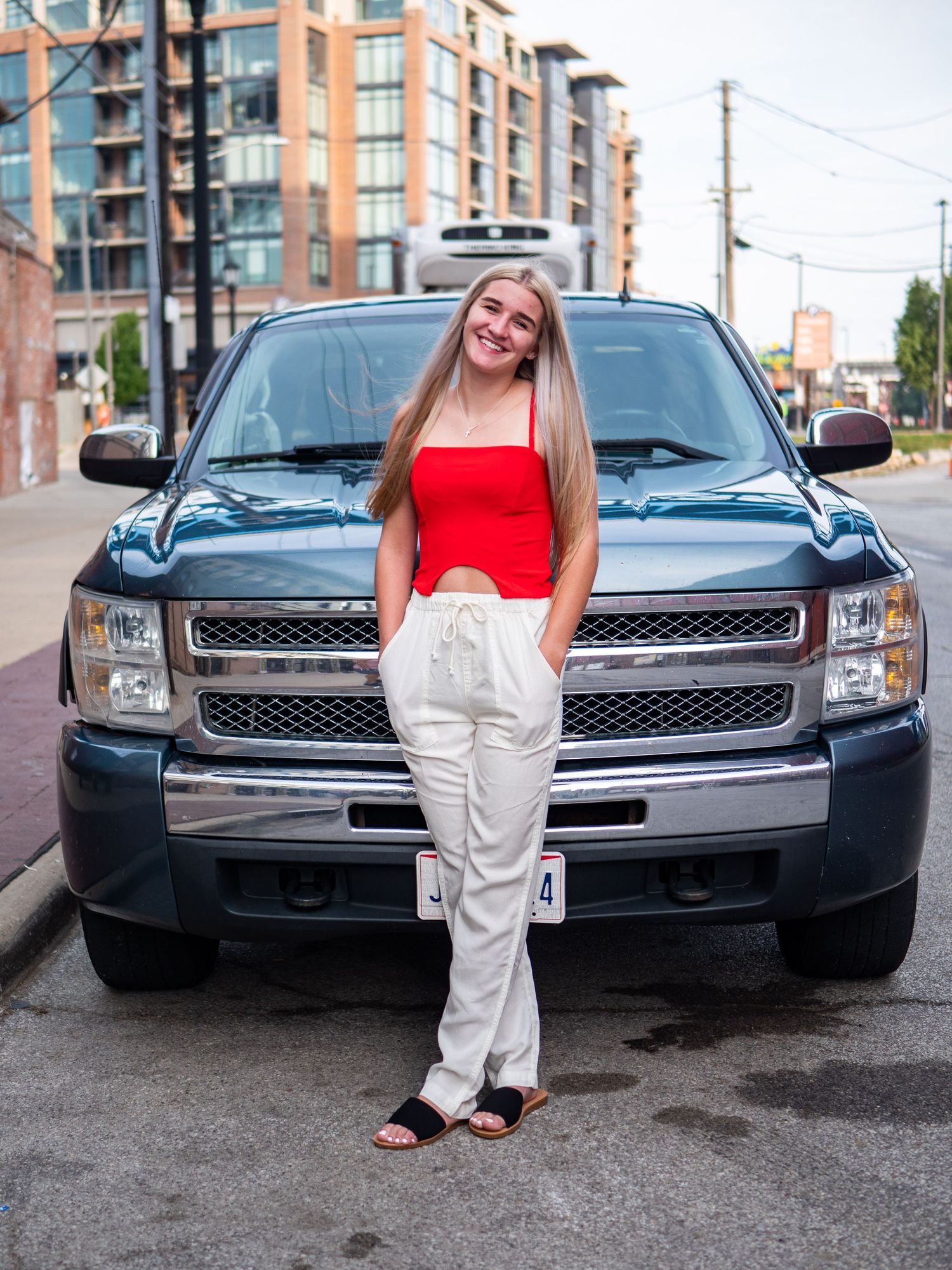 Red-dressed woman leaning against blue pickup truck in urban setting.