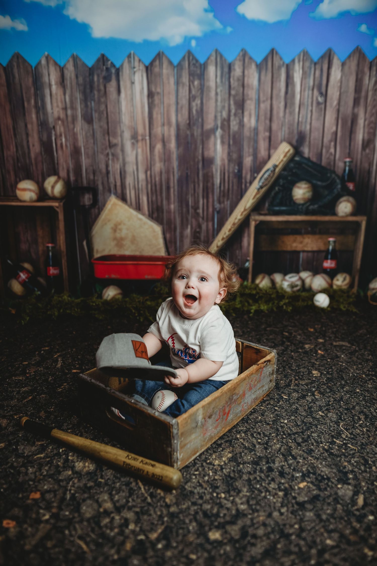 Laughing baby playing in wooden box with baseballs in backyard setting.