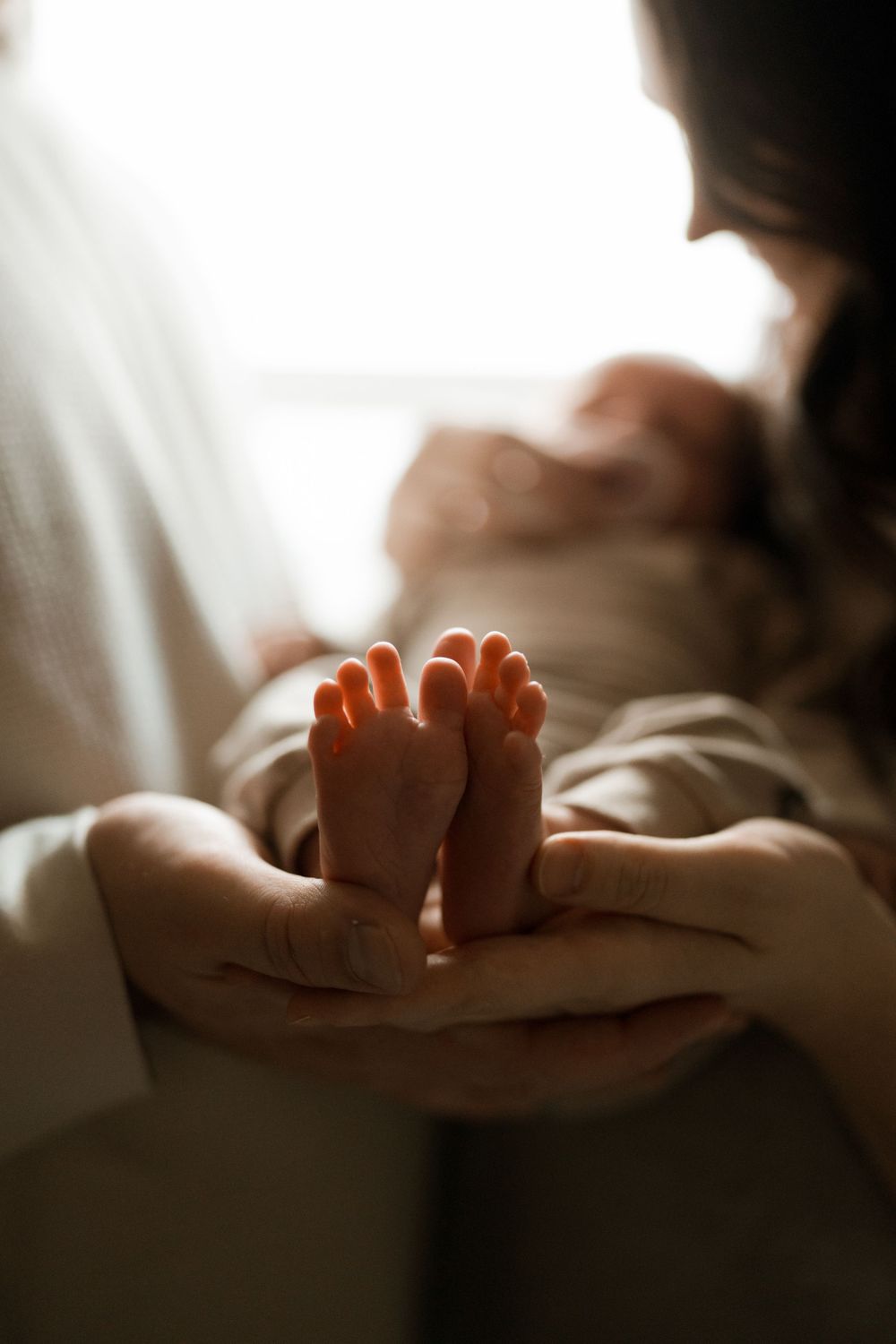 Tiny baby feet being gently held in caring hands in soft natural lighting.