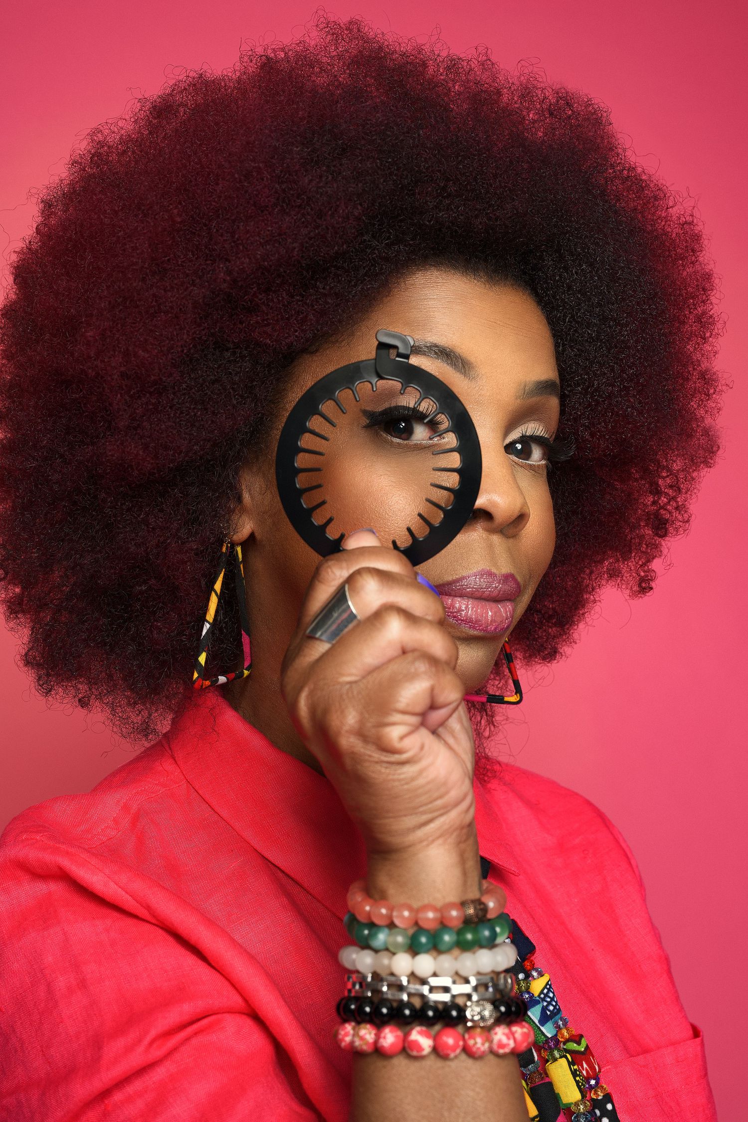 Creative portrait with magnifying glass against pink background wearing colorful accessories.