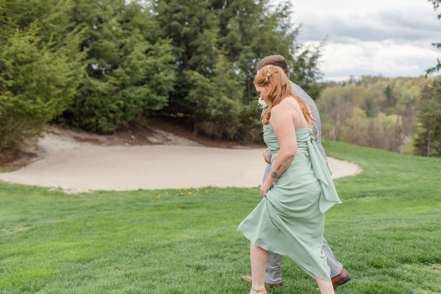Bridesmaids in mint green dresses twirl and dance on a grassy hillside.