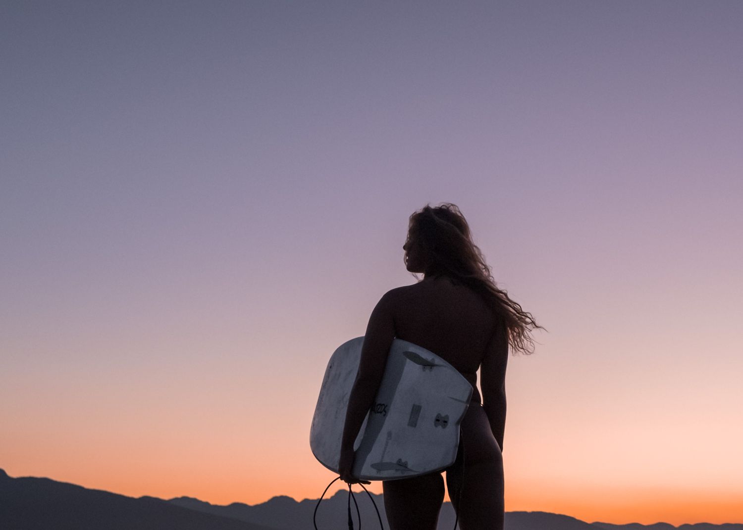 Woman at sunset holding surfboard, silhouette against pink sky, North Vancouver photographer
