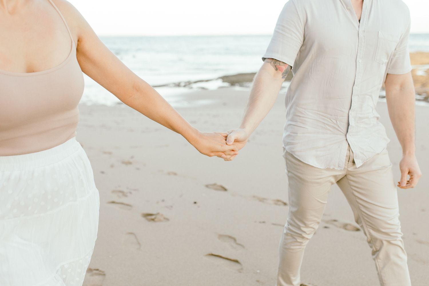 Close-up of hands holding while walking along the shoreline.