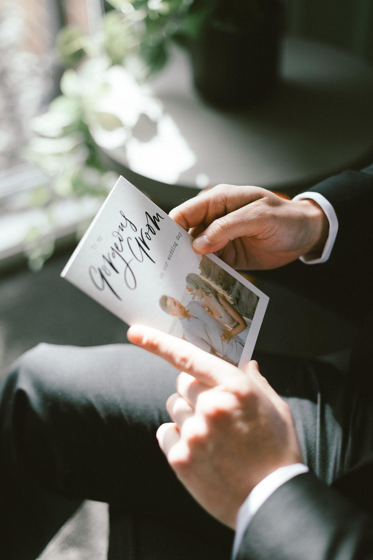 Hands holding a wedding card and photo in an intimate indoor setting.