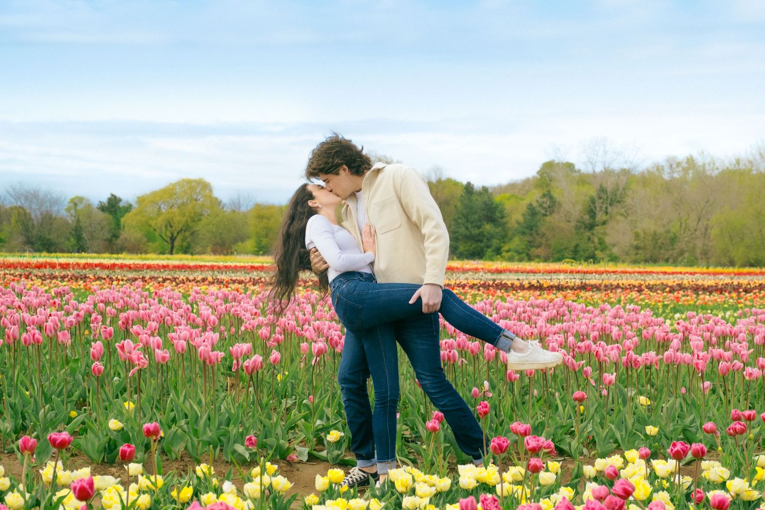 A romantic couple shares an intimate moment among colorful blooming tulips in a spring field.