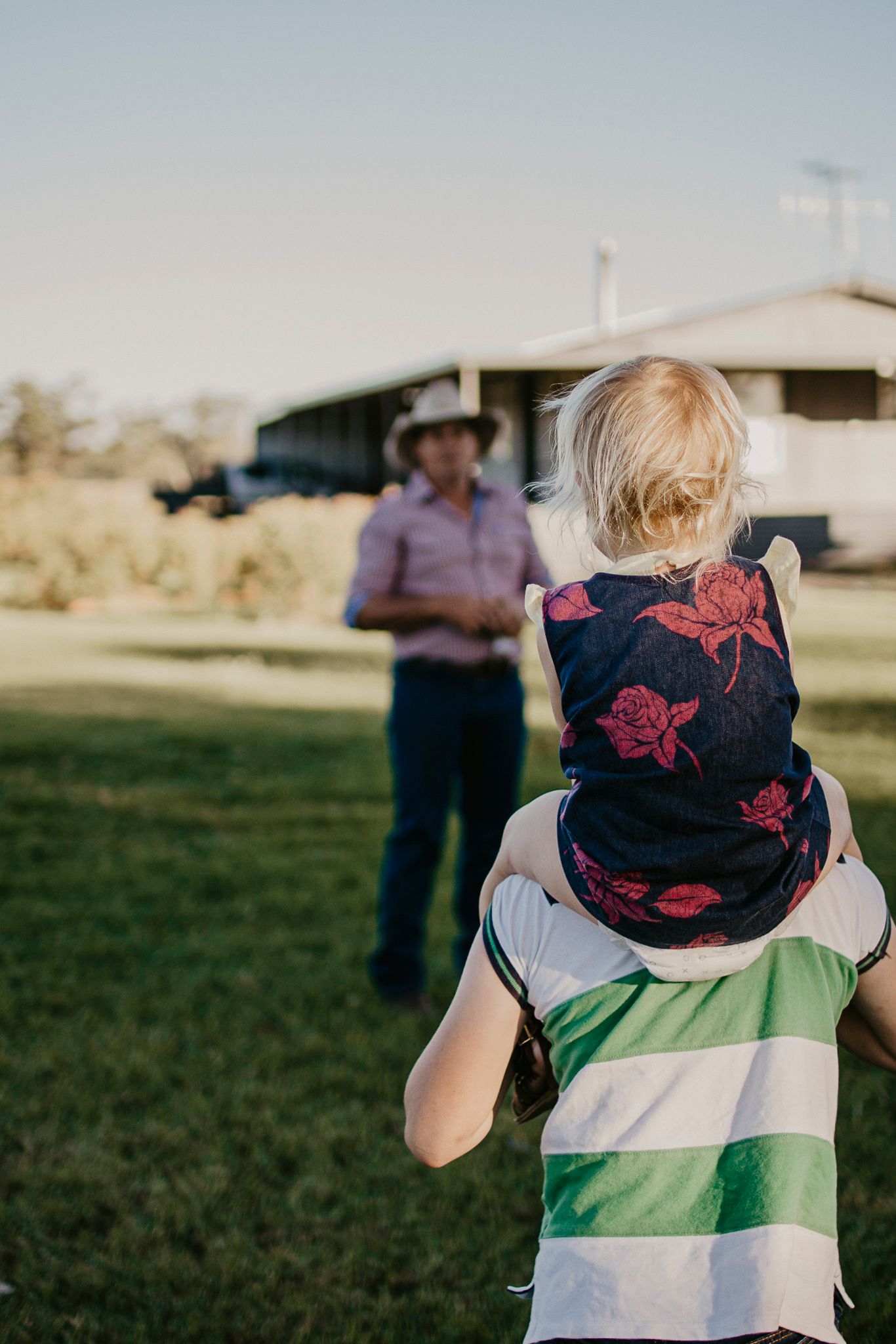 The family home in the background with the dad, looking at his son giving his daughter a shoulder ride.