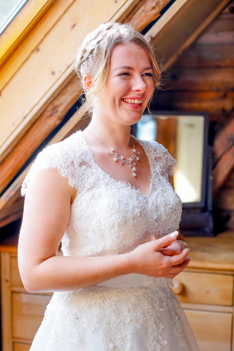 A bride radiates joy in her lace wedding dress and delicate jewelry.