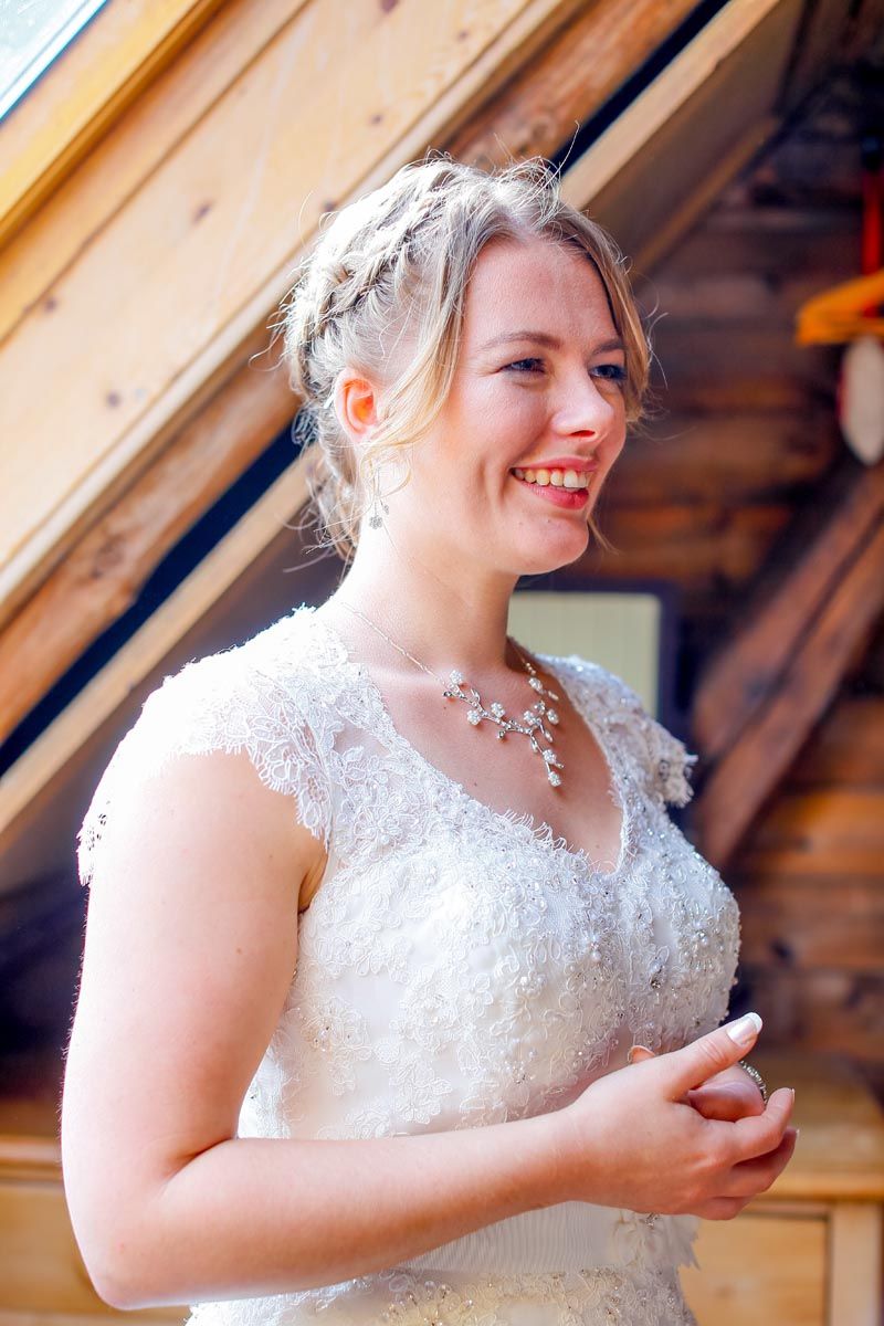 A bride in a delicate lace wedding dress smiles joyfully during her outdoor wedding.