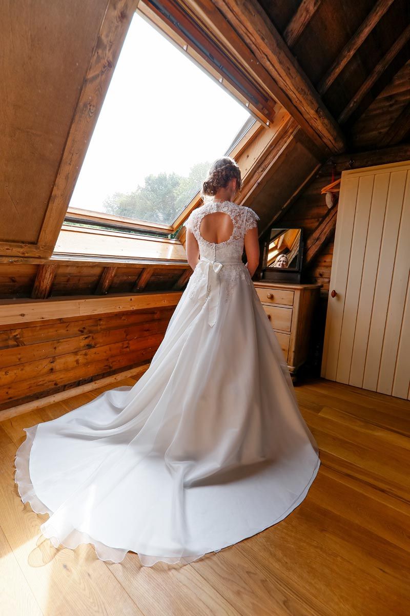 Full-length view of a wedding dress with train in rustic attic setting with skylight.