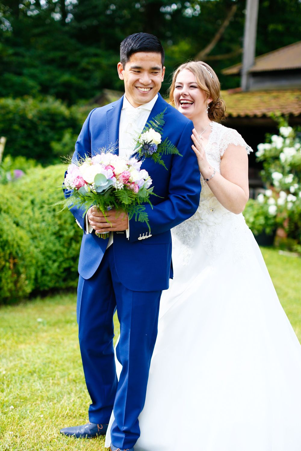Happy newlyweds share a joyful moment with pink bouquet in garden setting.
