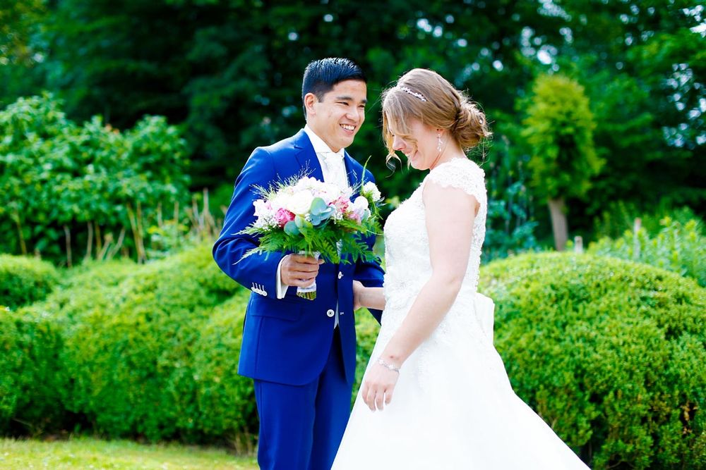 A happy wedding couple holding a pink and white bouquet in a lush garden setting.