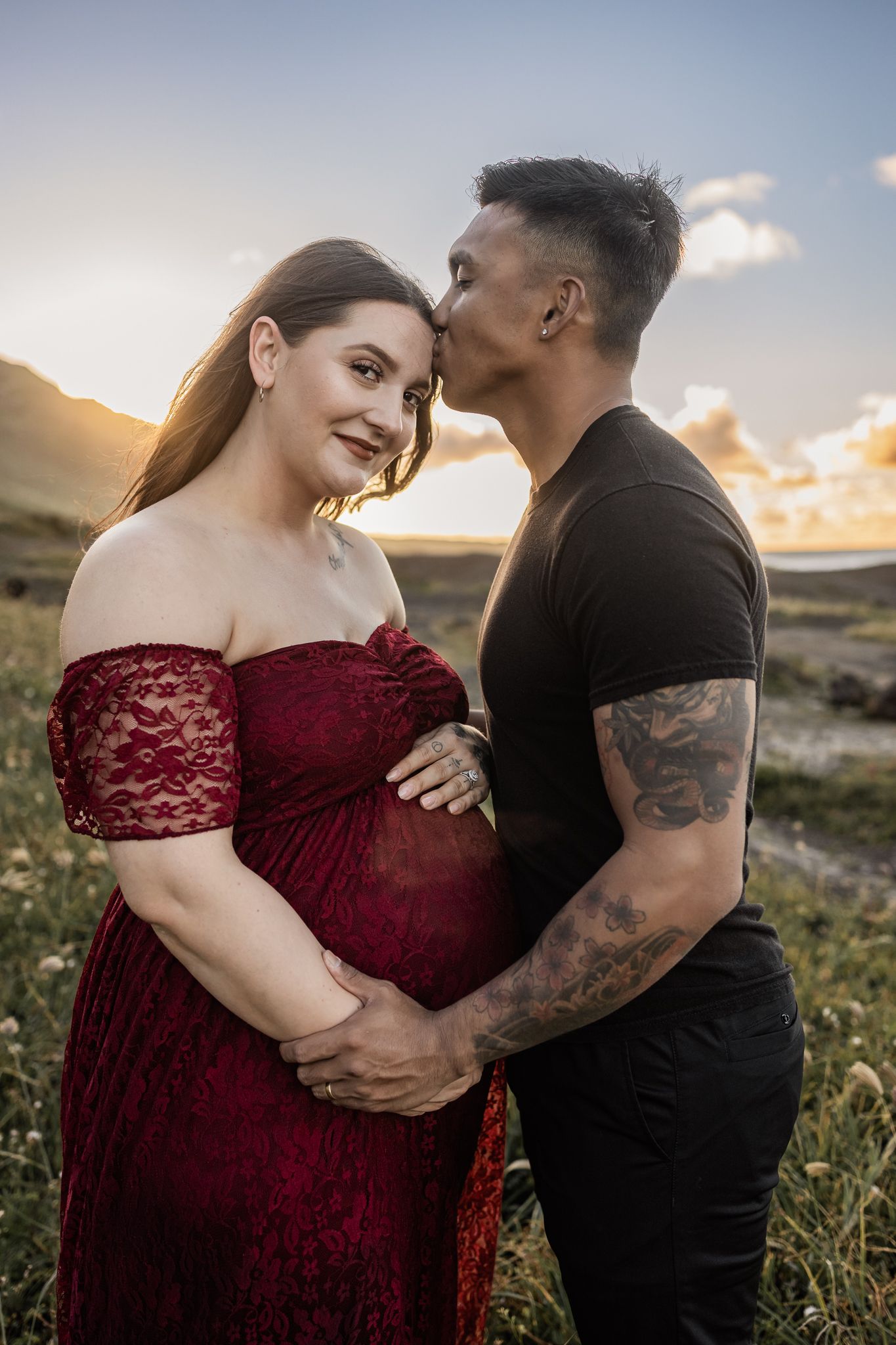 Couple shares intimate moment during maternity photoshoot at sunset.