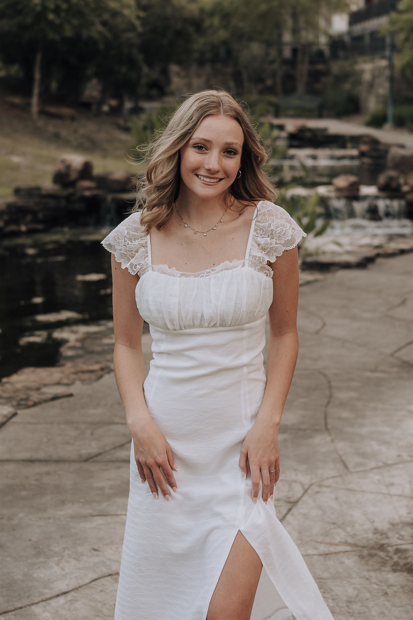 A white lace cap sleeve dress photographed outdoors near rocks and water.