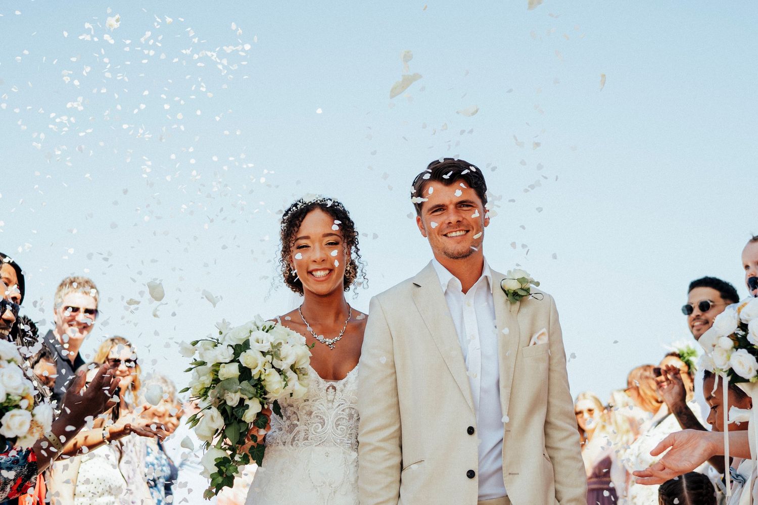 A celebratory wedding moment with confetti falling against a bright blue sky.