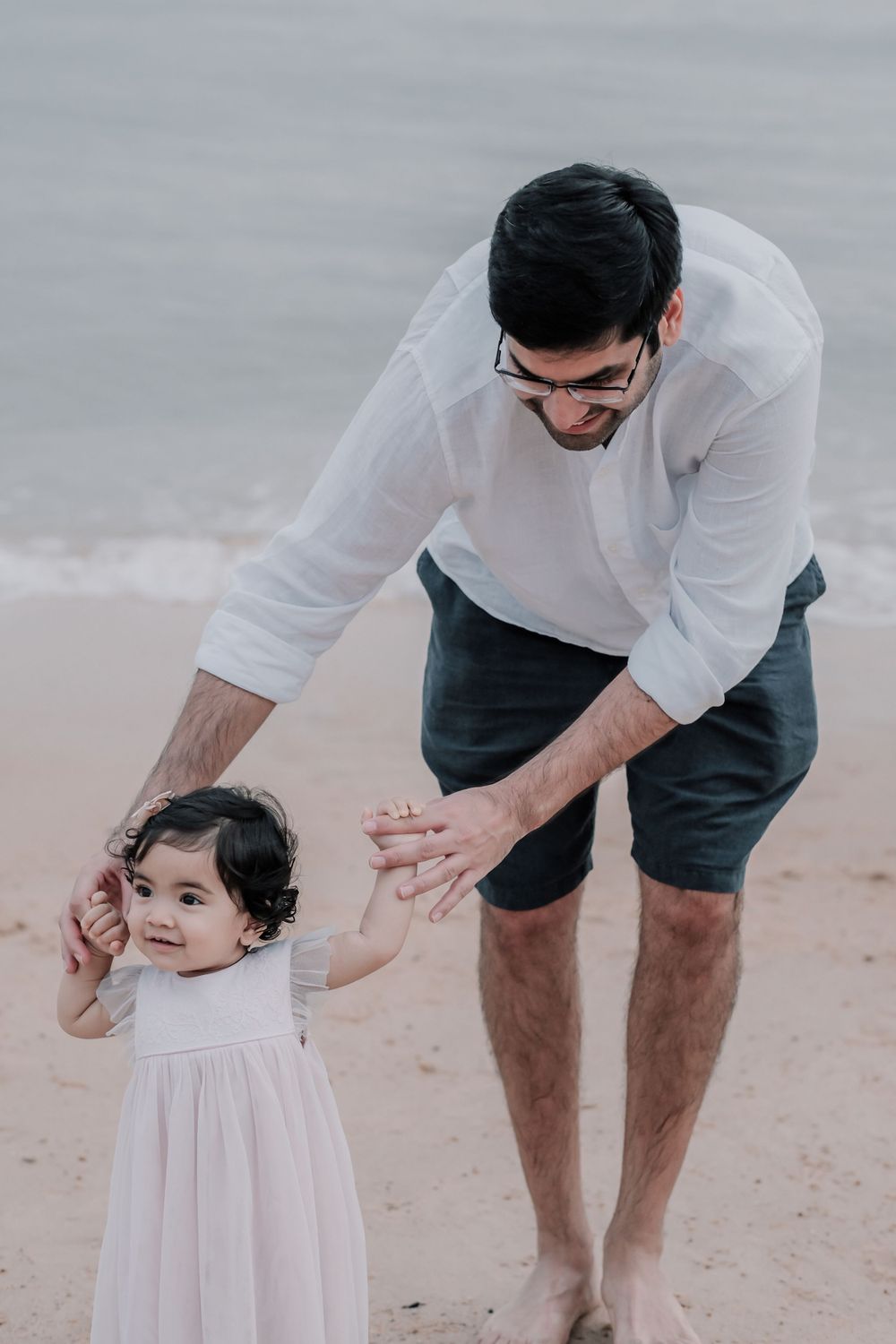 Parent and child holding hands while walking along the beach at dusk.