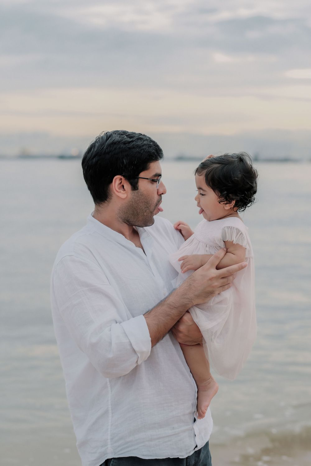 A tender moment between parent and child against an ocean backdrop at sunset.