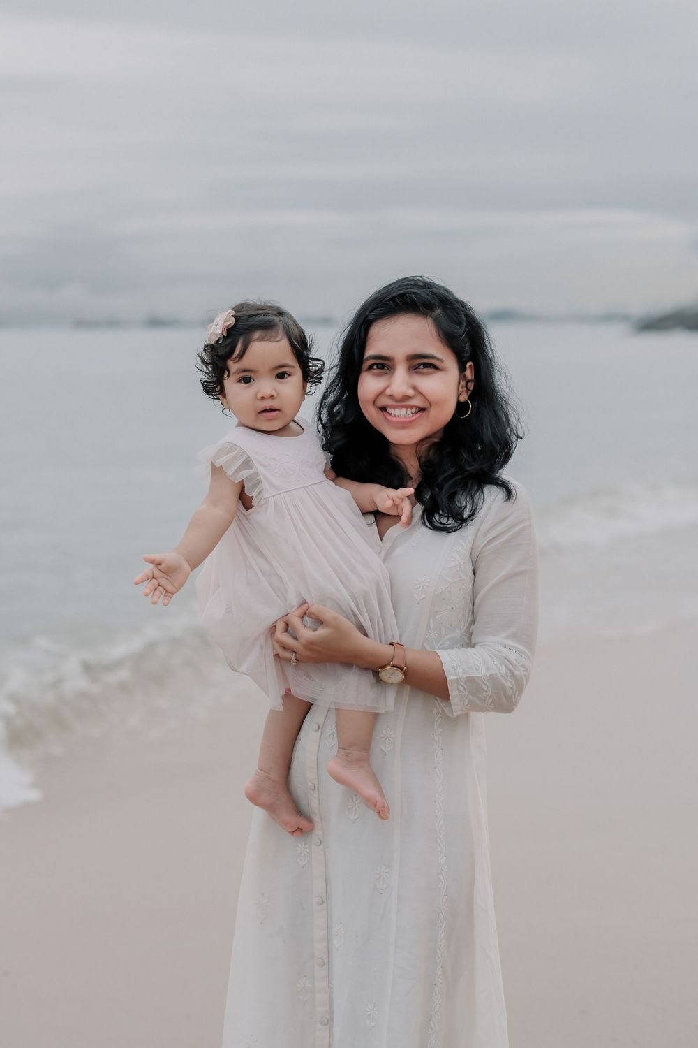 Parent and child in matching white outfits share a joyful moment on the beach.