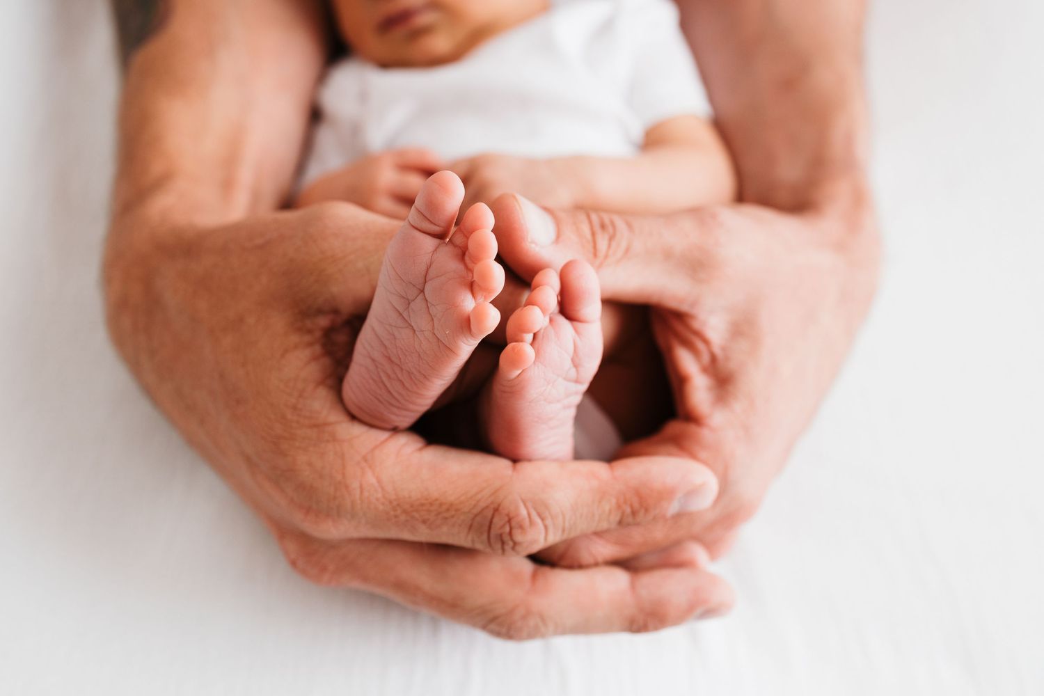 Hands gently holding and examining a small baby's feet against a white background.