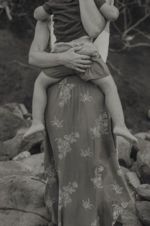 Black and white photo of a mother holding her baby while standing on rocks.