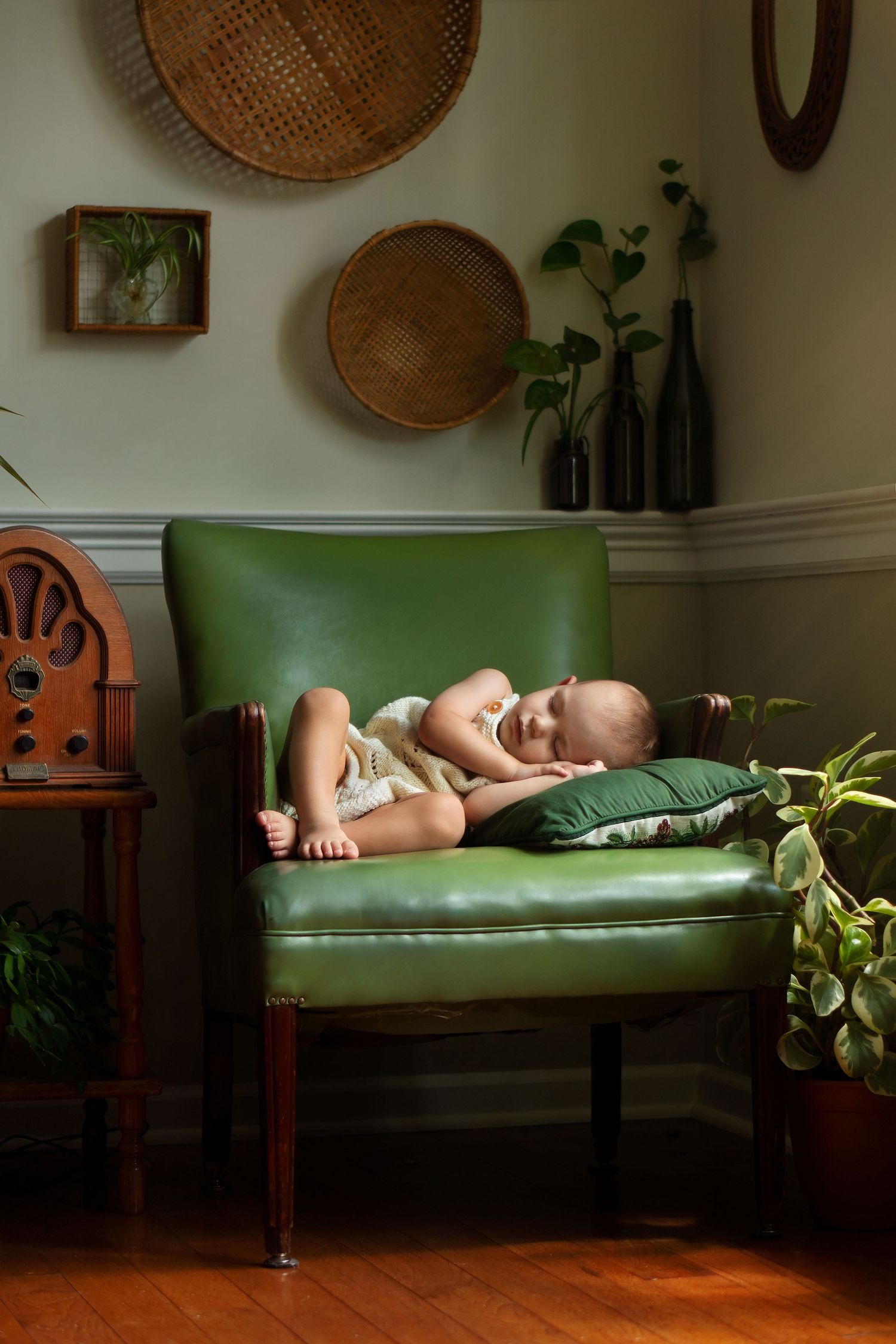 baby sleeps in green leather chair surrounded by houseplants