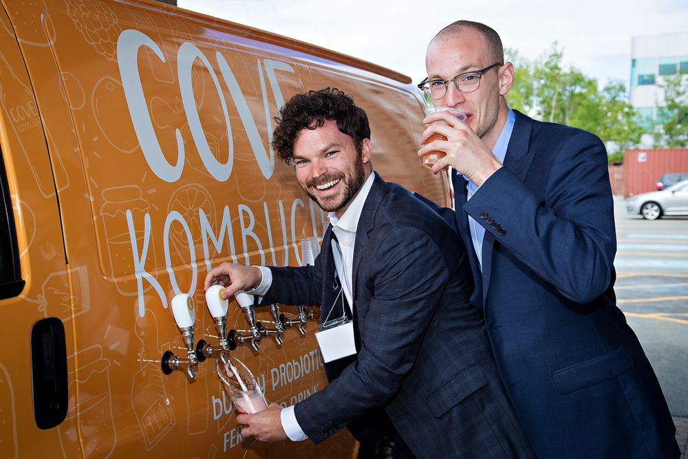 Two men pose while pouring drinks from a Cove Kombucha van.
