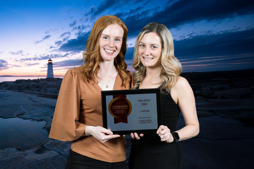 Two people pose with a plaque with the peggys cove lighthouse in the background.