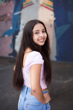 High school senior girl standing in front of downtown mural looking over shoulder at the camera.