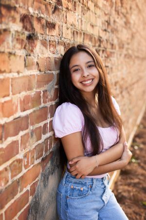 High school senior girl leaning against brick wall with sunsetting behind her.