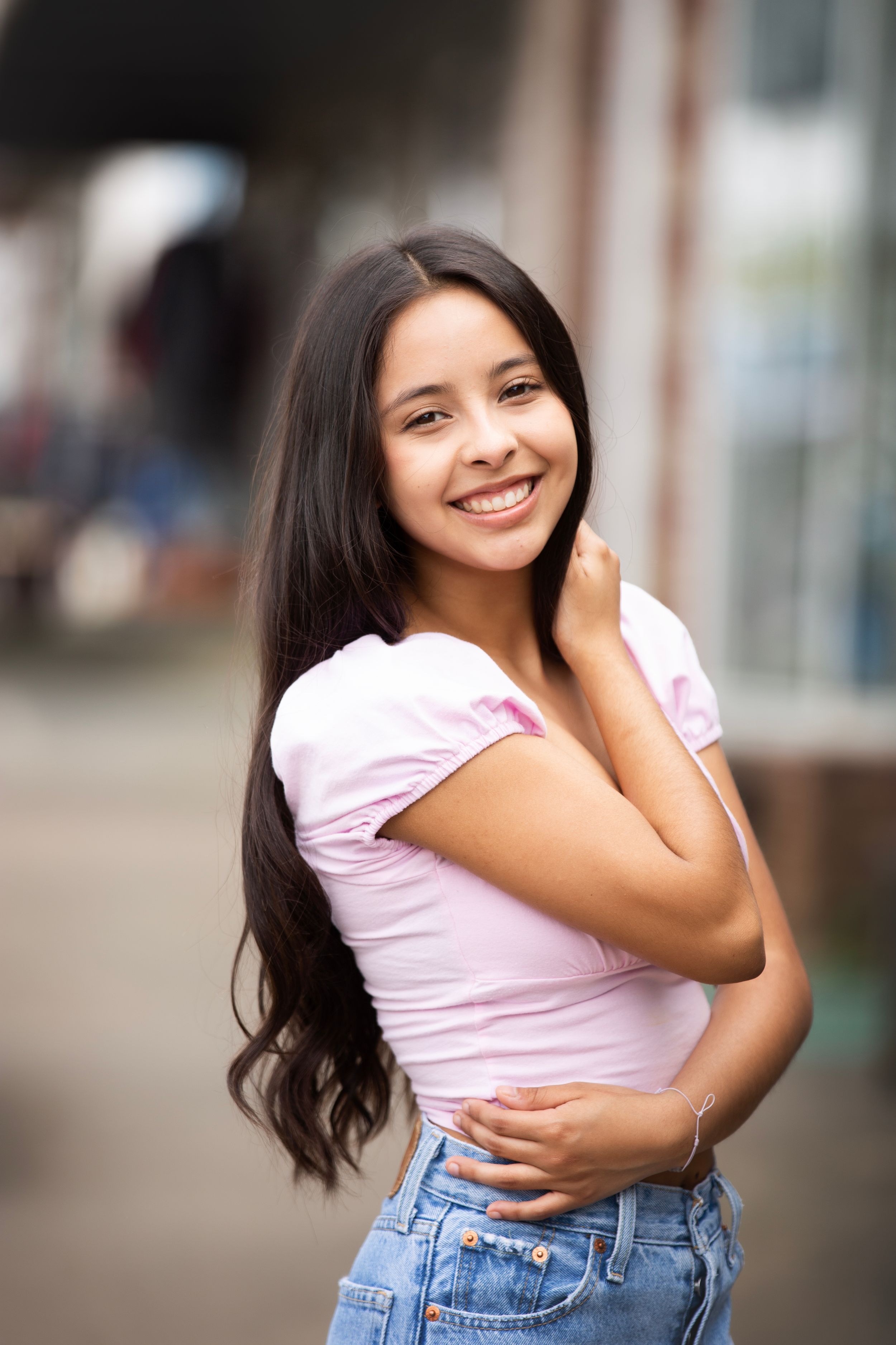 High School Senior girl wearing pink shirt and jeans on a downtown street.