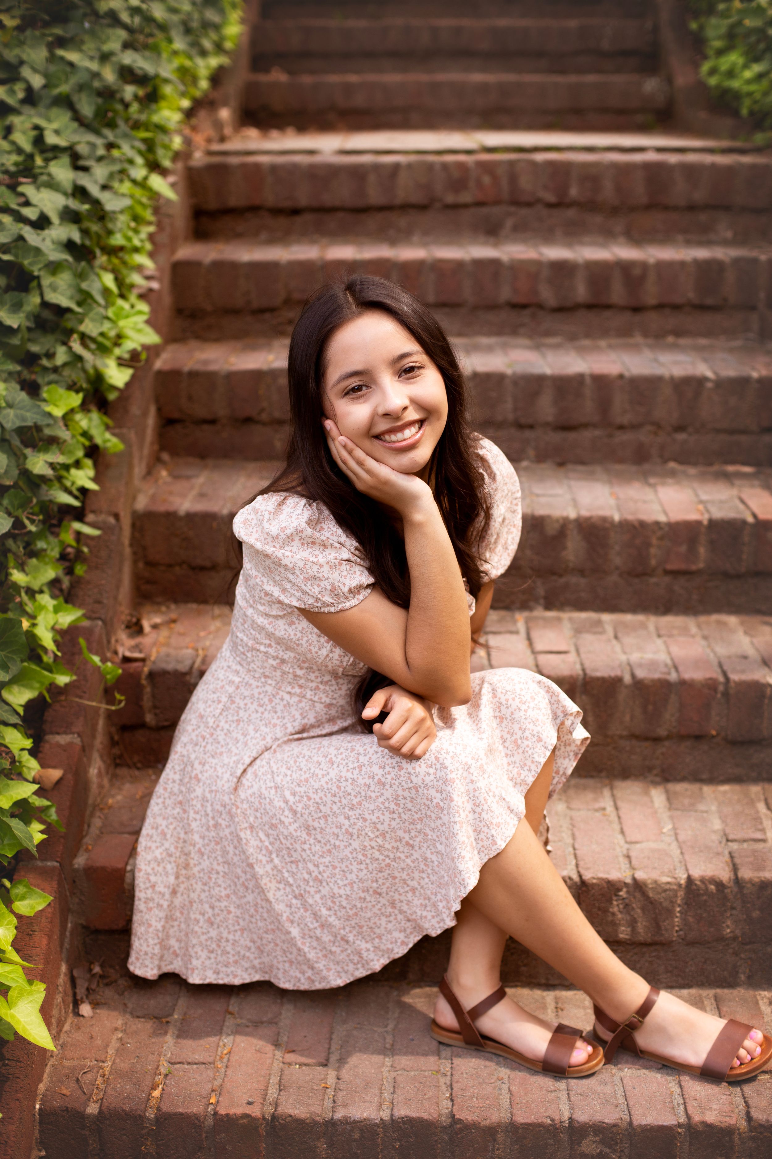High School Senior girl wearing a floral dress sitting on brick steps.