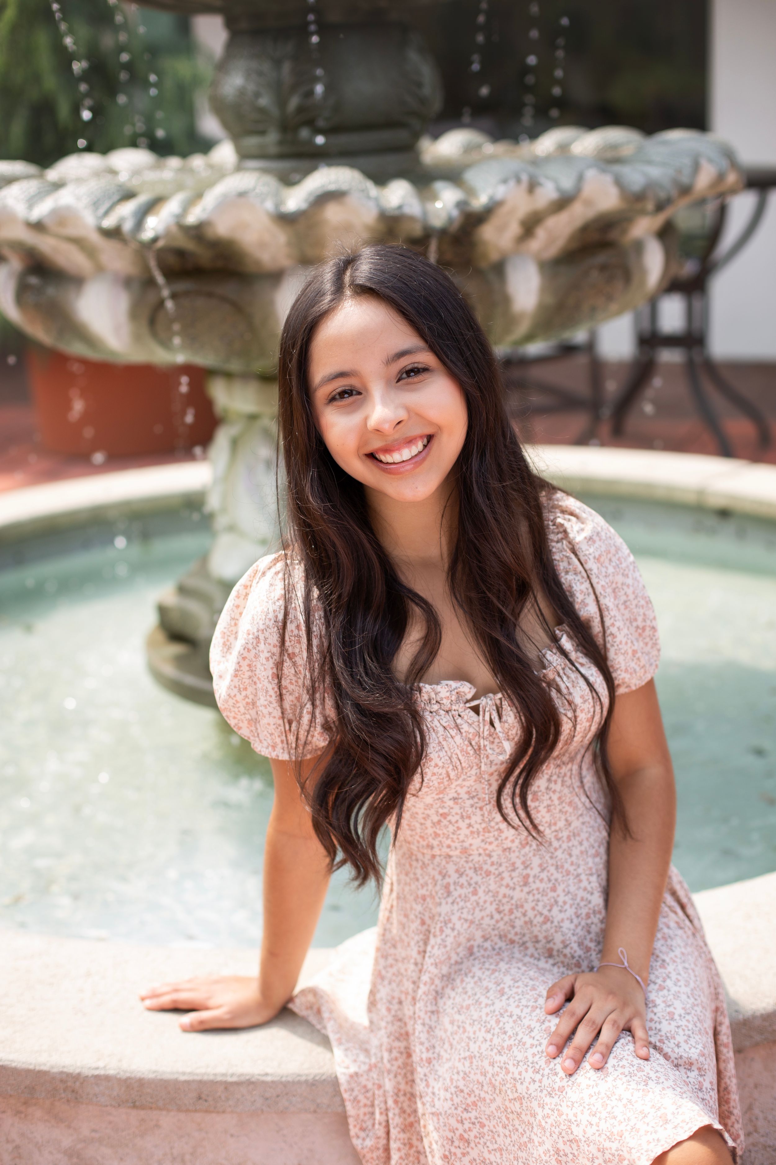 High School Senior girl wearing a floral dress sitting on the edge of a water fountain.