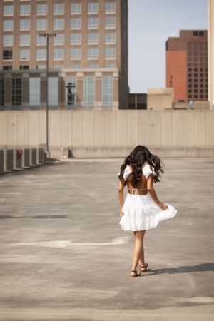 High School Senior in white dress on the top of a parking garage walking away from camera.
