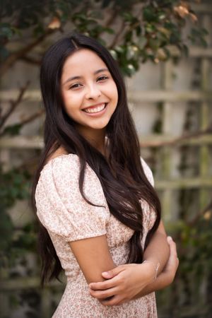 High school senior girl in floral dress headshot with garden lattice in the background.