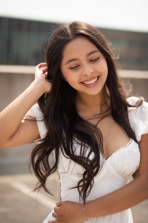 High school senior girl wearing a white dress, pulling her hair out of her face.