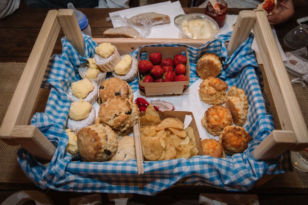 A rustic wooden tray filled with pastries, scones and fresh strawberries on a blue checkered cloth.