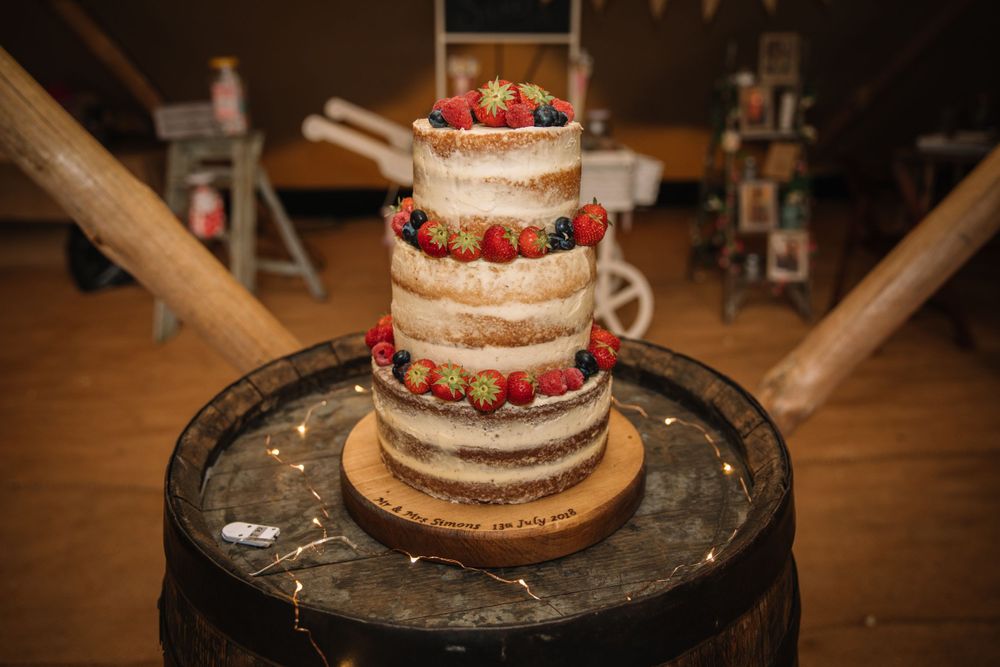 Naked wedding cake decorated with fresh strawberries and blueberries on dark wooden barrel.