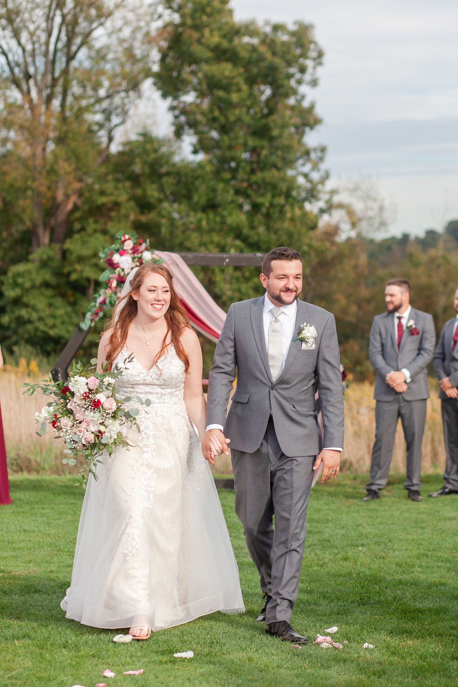 A joyful wedding couple walks hand in hand across a grassy lawn after their outdoor ceremony.