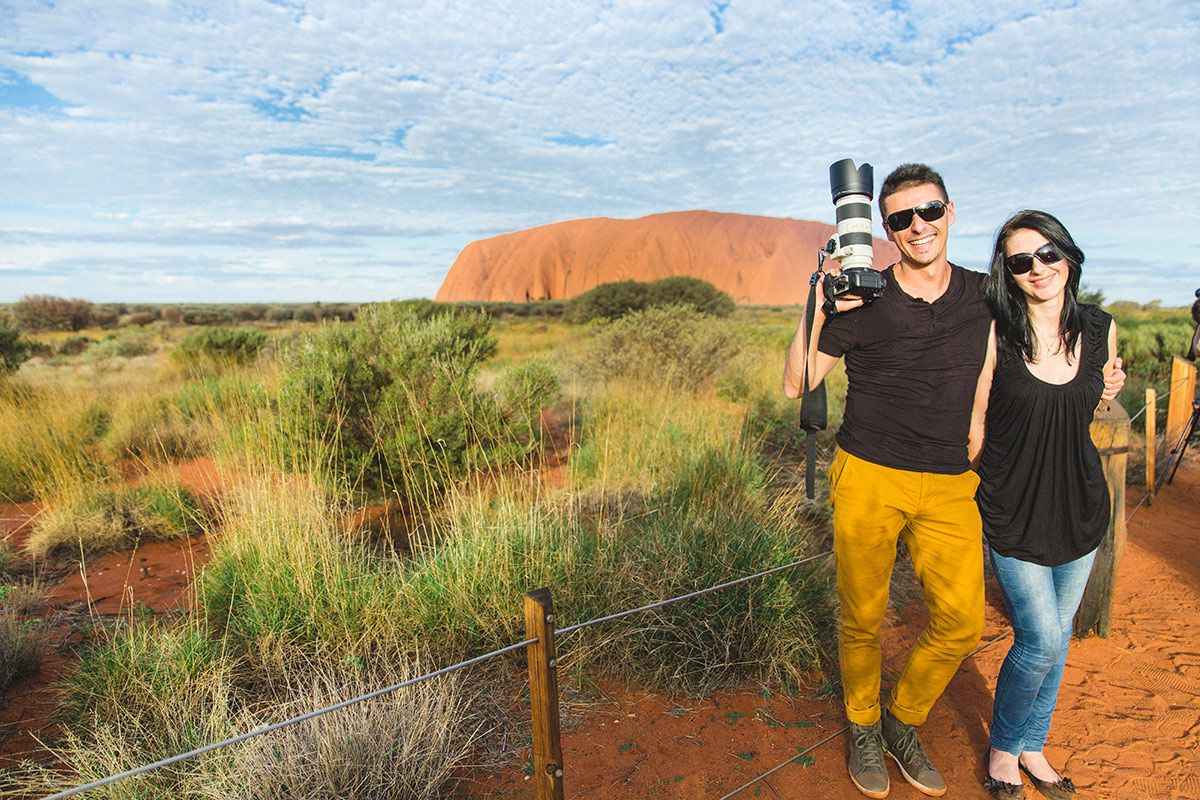 A series of travel photos showing people exploring the red rocks and desert landscape of Uluru in Australia.