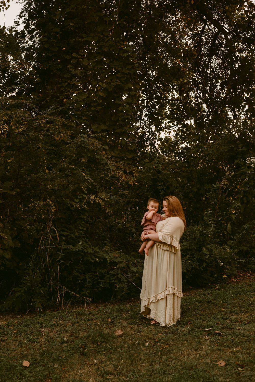 Two figures stand among autumn trees during golden hour photoshoot.