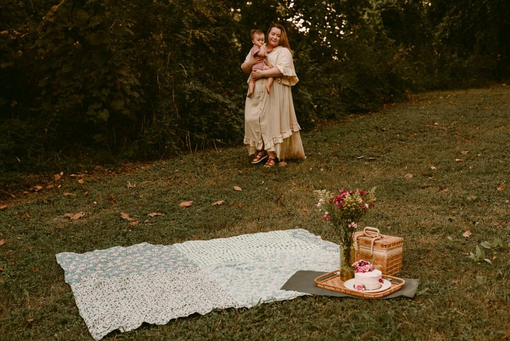Outdoor picnic setup with white blanket and figures standing among autumn trees.