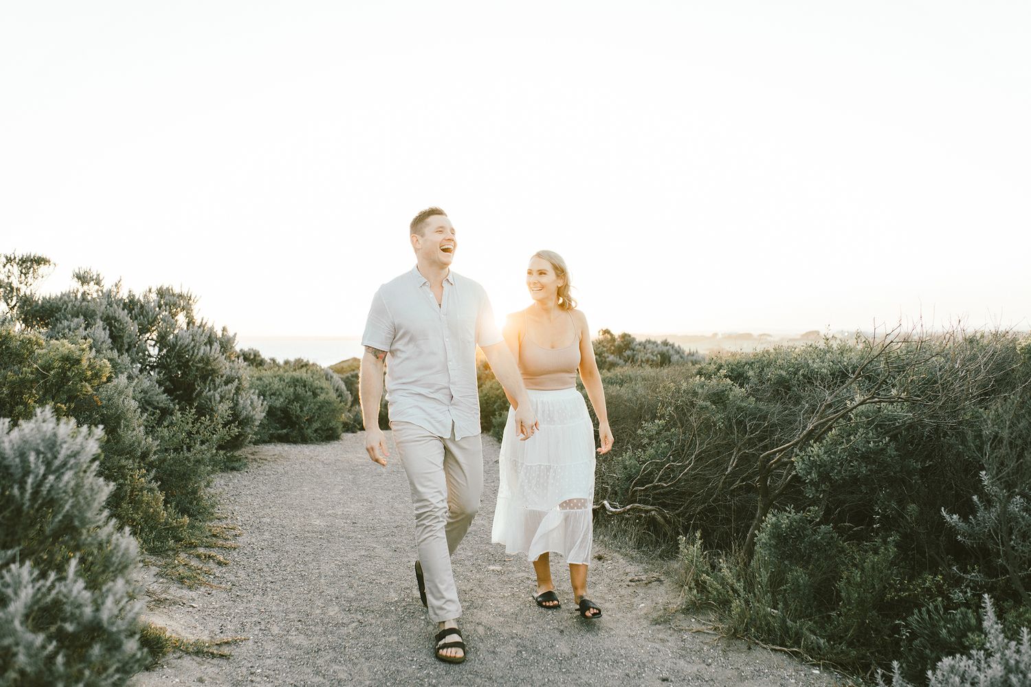 A couple walks along a coastal trail during golden hour sunset.