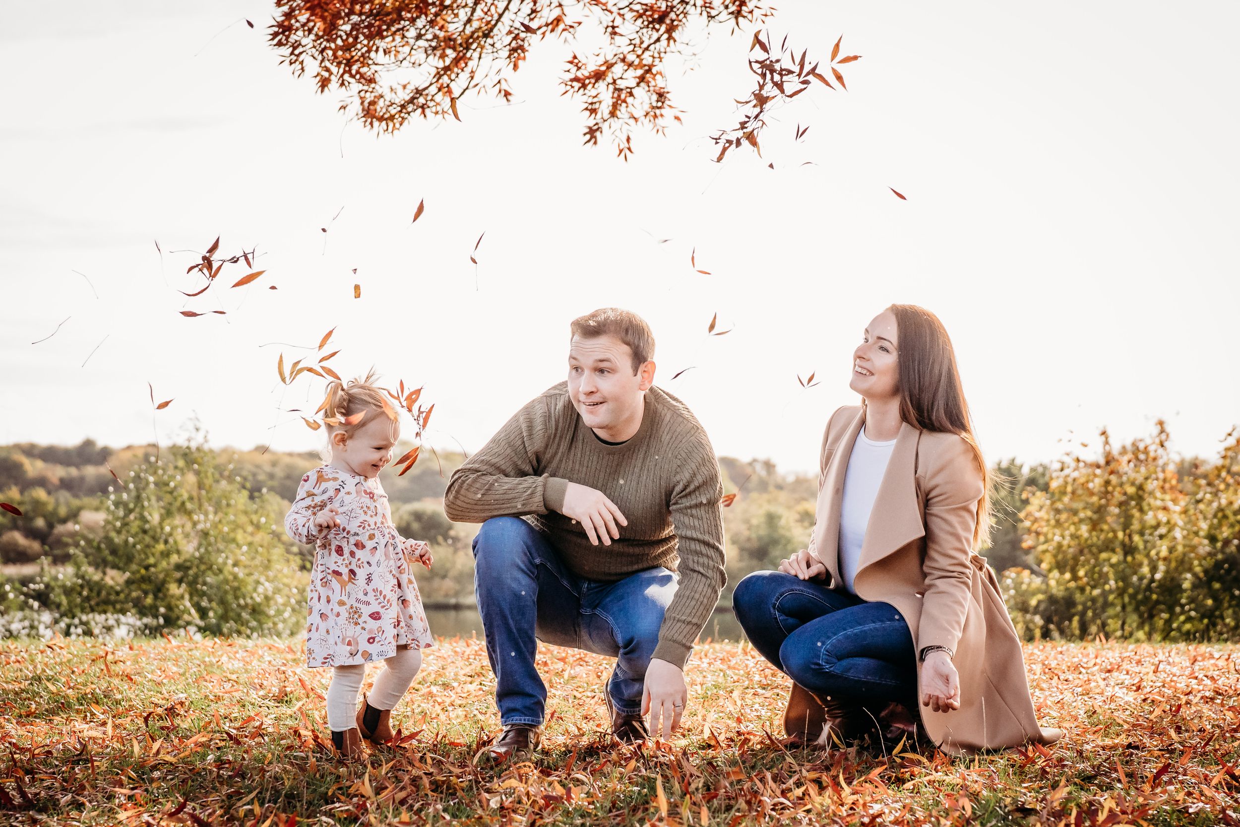 Family playing in fallen autumn leaves under colorful tree.