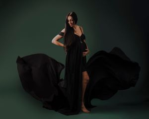 A dramatic fashion portrait of a woman in a flowing black dress against a dark green background.