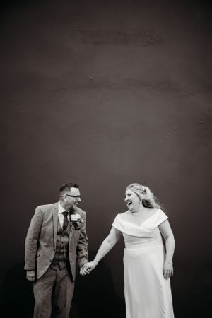 Black and white candid moment of newlyweds laughing against dark background.