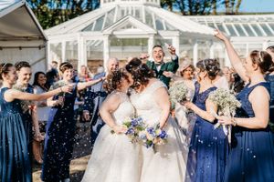 A celebratory wedding party throws confetti at a couple under a white tent structure.