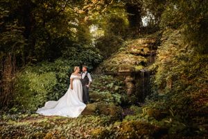 A dreamy forest wedding scene with a couple in formal attire standing among lush greenery and natural stone steps.