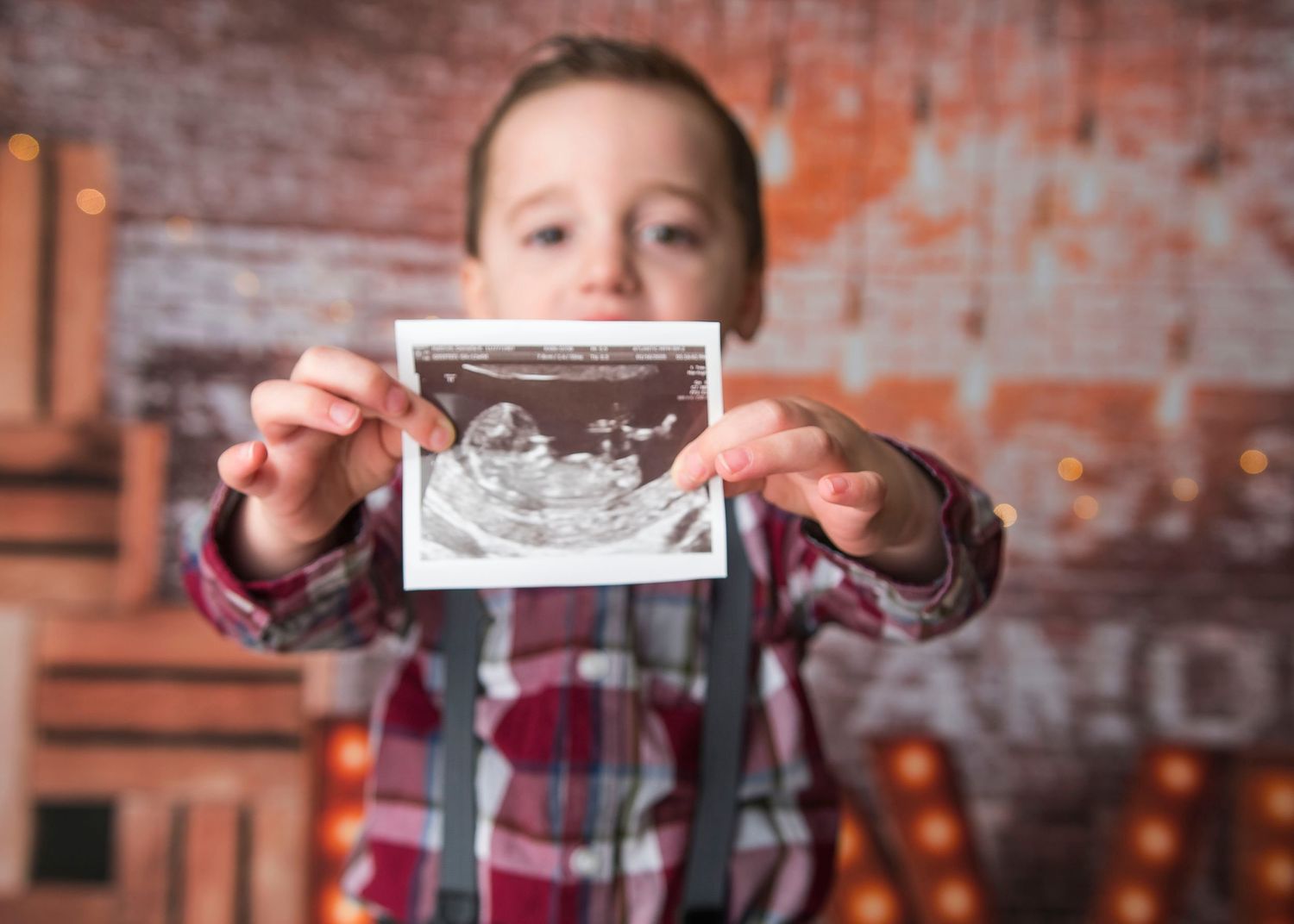 A person holding up an ultrasound photo against a rustic brick wall with glowing letters.