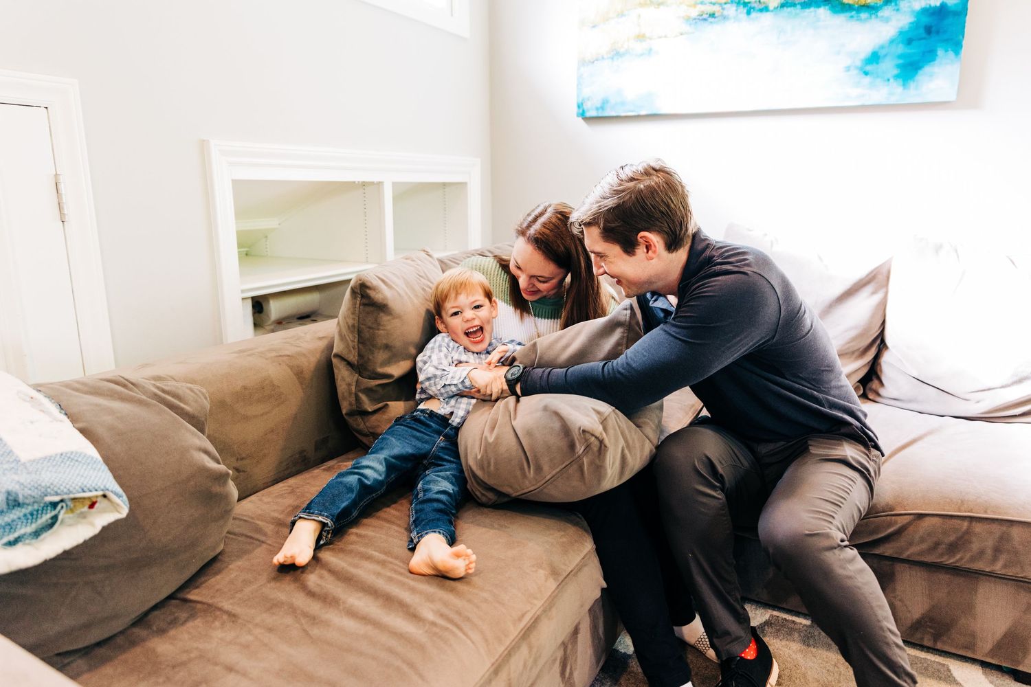 Young boy laughing while mom and dad tickle him on the couch