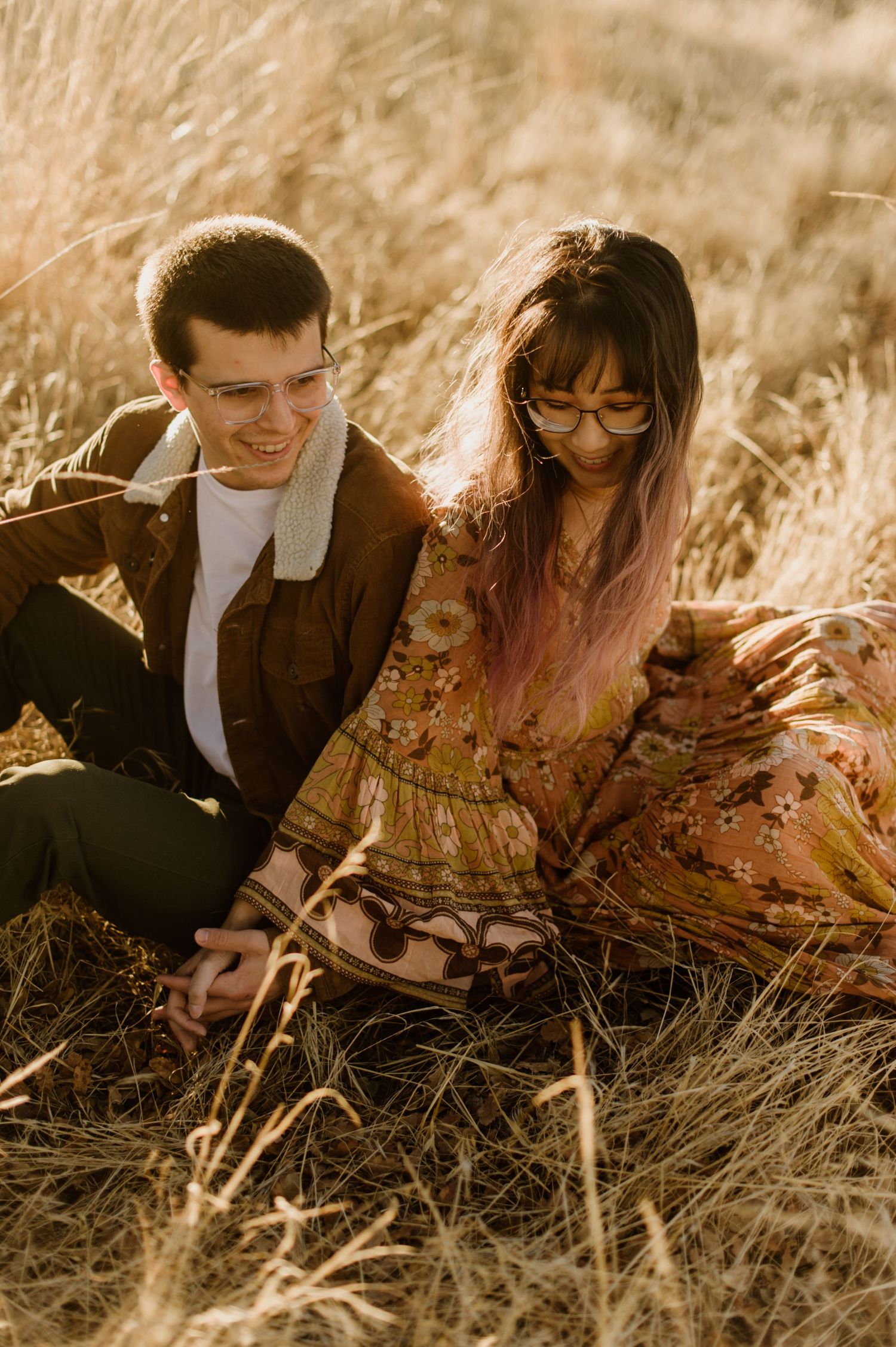 A couple sits together in a golden wheat field during sunset in warm vintage tones.